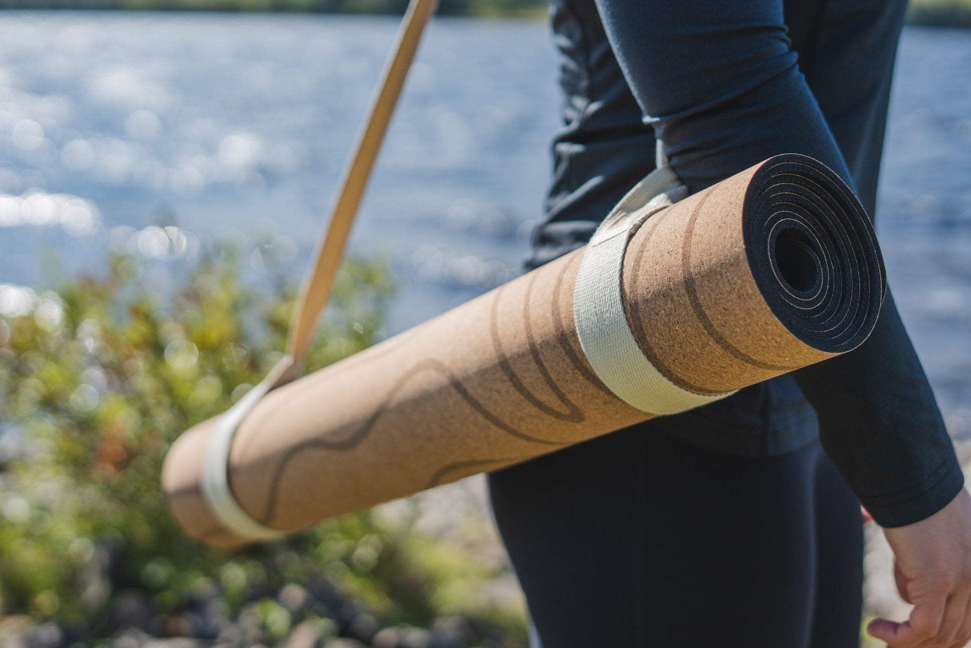 ROOTD Elite Terra Design. Non-toxic eco cork exercise mat topographical topo map design. Rolled up and carried on the shoulder of a woman with a white carry strap. 