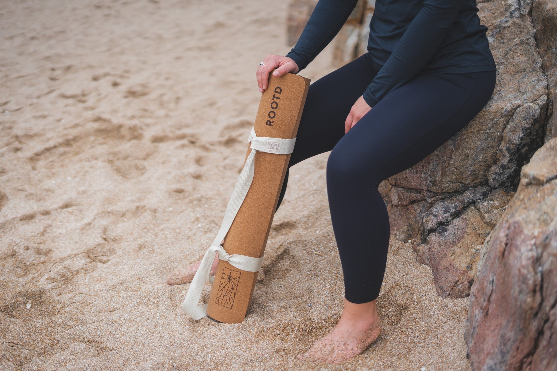 ROOTD Elite Bare Design. Non-toxic eco cork exercise mat rolled up with a white cotton carry strap at the beach. 