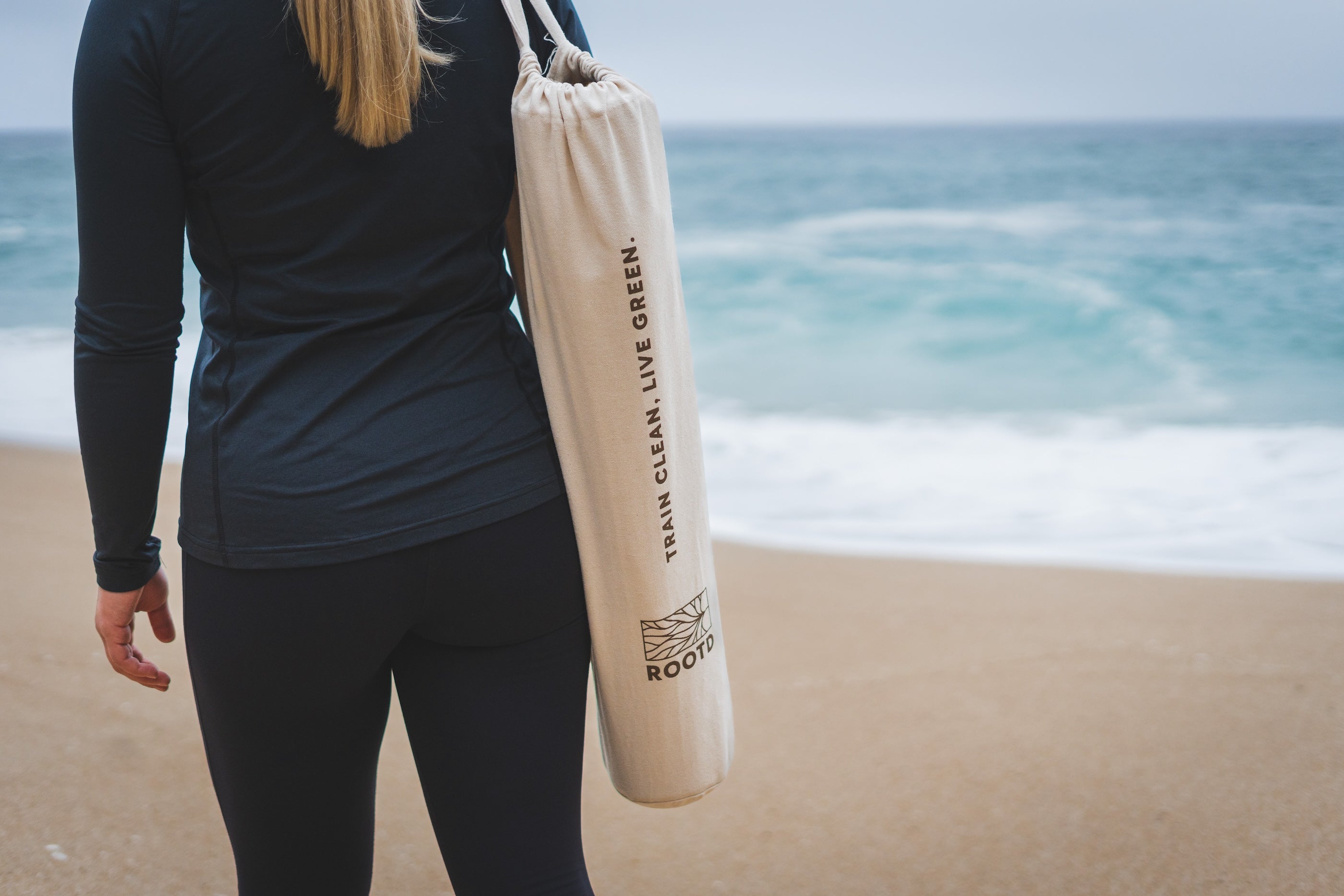 ROOTD elite mat non-toxic eco cork exercise mat in a carry bag being carried by a woman at the beach